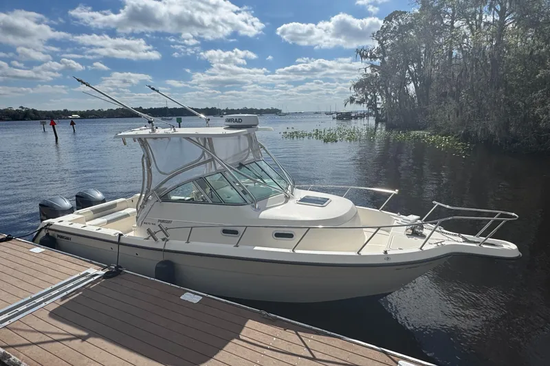 Slide: The Image of 1999 Pursuit 2870 Walkaround boat docked on a sunny lake with trees in the background. - 15
