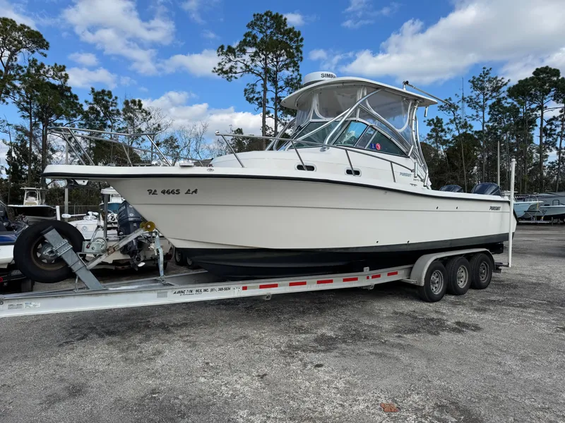 Slide: The Image of 1999 Pursuit 2870 Walkaround boat on a trailer, parked outdoors under a blue sky. - 40