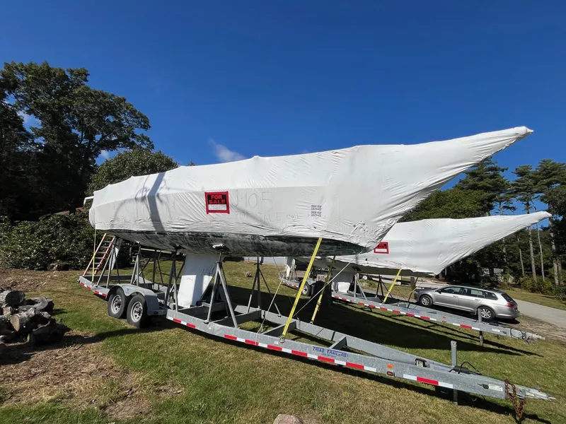 Slide: The Image of 2001 J Boats J/105 sailboats covered on trailers, parked on grass under a clear blue sky. - 22