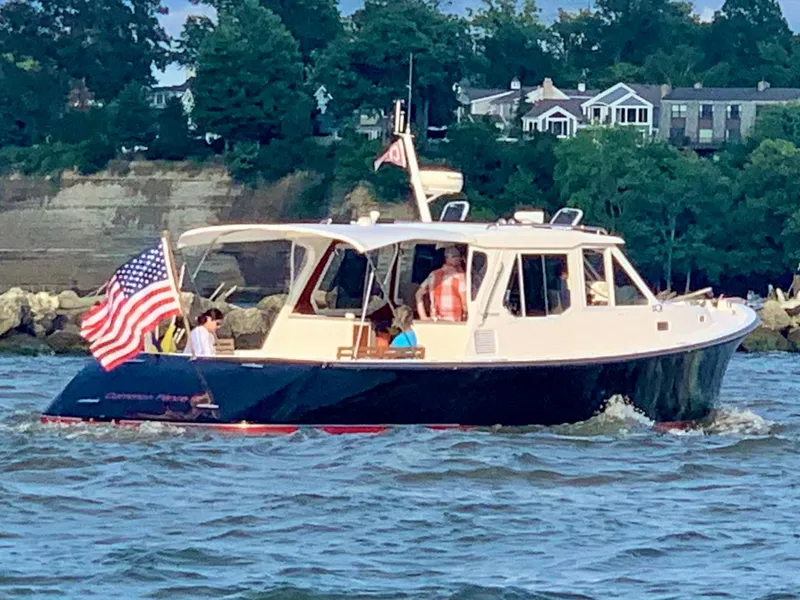 Slide: The Image of 2005 True North 38 Heritage boat cruising with American flag, near shoreline houses. - 3