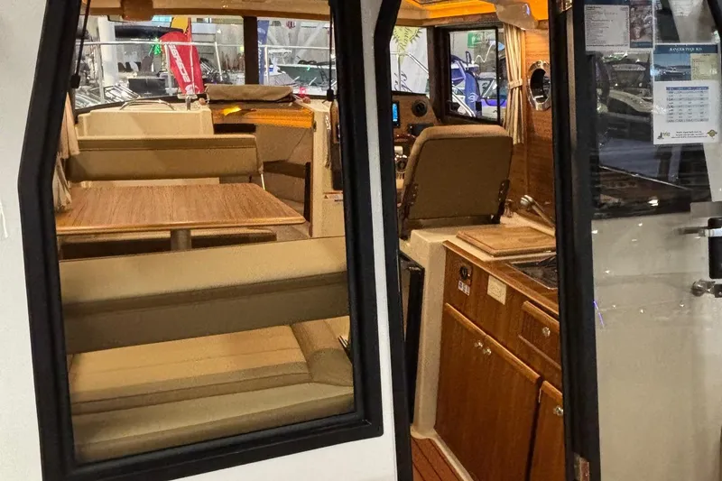 Slide: The Image of Interior view of 2025 Ranger Tugs R-23, featuring seating and wooden cabinetry. - 14