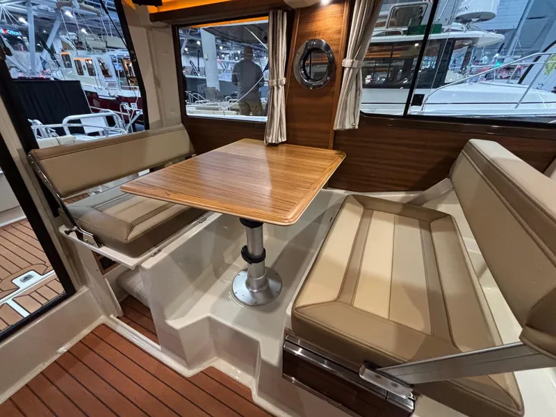 Slide: The Image of 2025 Ranger Tugs R-23 interior with wood table, beige seating, and large windows. - 5