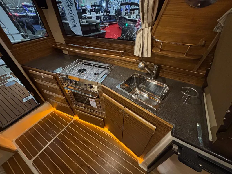 Slide: The Image of 2025 Ranger Tugs R-29 S interior kitchen with wood finish, stove, and sink. - 14