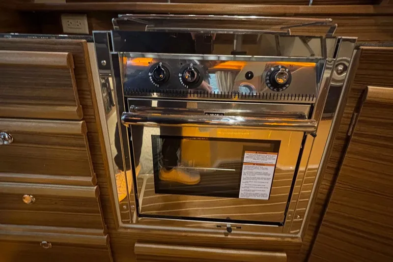 Slide: The Image of 2025 Ranger Tugs R-29 S kitchen oven with wooden cabinetry and stainless steel finish. - 15