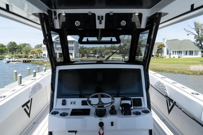 Slide: The Image of 2025 Twin Vee 400 GFX2 CC boat interior with steering console, docked by waterfront homes. - 18