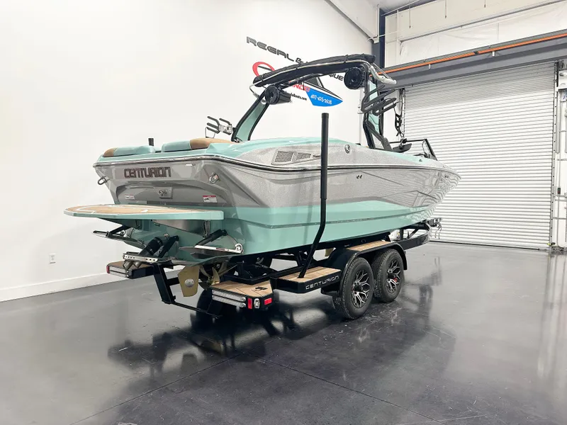 Slide: The Image of 2025 Centurion NV233 boat in showroom, teal and gray design, on a dual-axle trailer. - 2