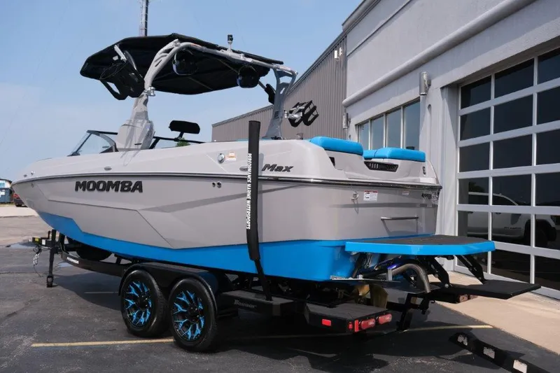 Slide: The Image of 2025 Moomba Max boat on trailer, gray and blue design, parked outside a building. - 3