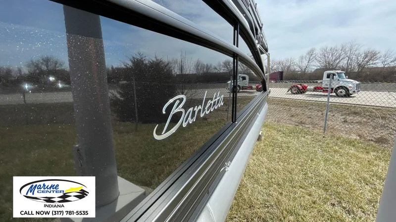 Slide: The Image of 2025 Barletta Aria A24UC pontoon boat side view with logo, parked near a fence. - 10