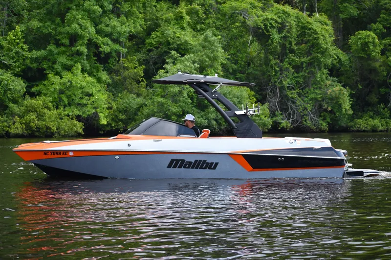 Slide: The Image of 2020 Malibu Wakesetter 22 MXZ boat on a calm lake with lush green trees. - 0
