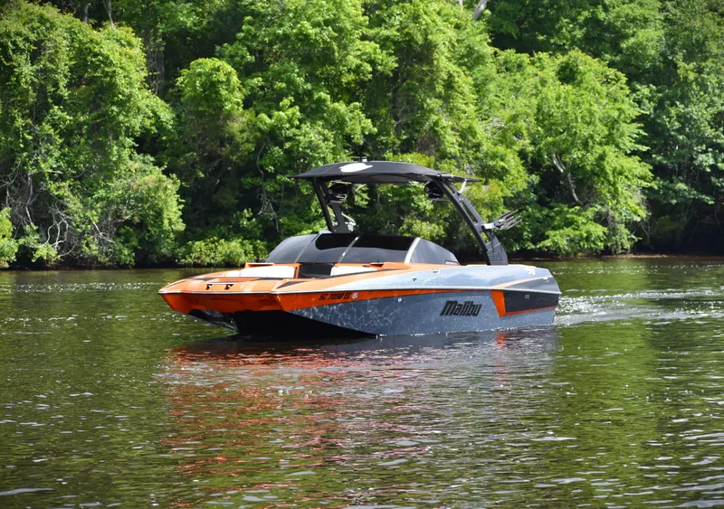 Slide: The Image of 2020 Malibu Wakesetter 22 MXZ boat on a calm river, surrounded by lush greenery. - 14