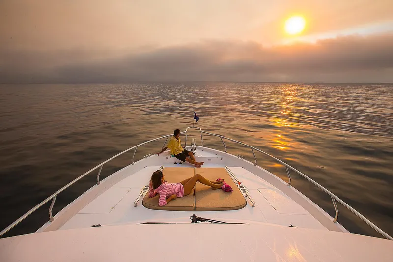 Slide: The Image of 2026 Hampton 650 Pilothouse yacht at sunset, with people relaxing on deck. - 24