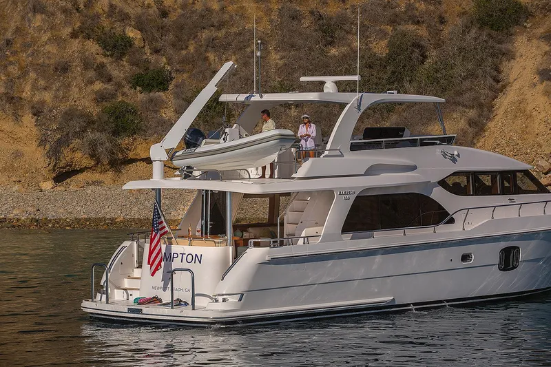 Slide: The Image of Luxury 2026 Hampton 650 Pilothouse yacht cruising near rocky shoreline. - 25
