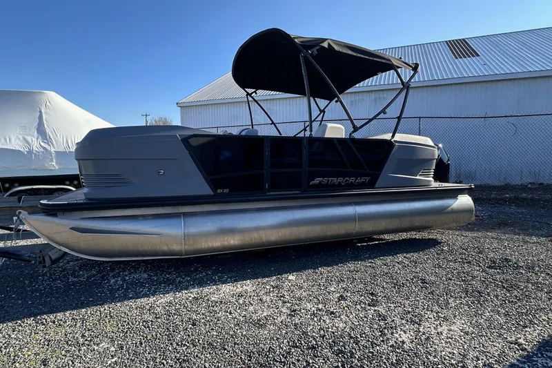 Slide: The Image of 2025 Starcraft GX 20 R DH pontoon boat with canopy, parked on gravel. - 4