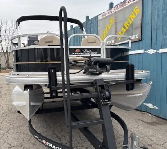 Slide: The Image of 2021 Sun Tracker Bass Buggy 16 XL pontoon boat on trailer, parked near blue fence. - 2