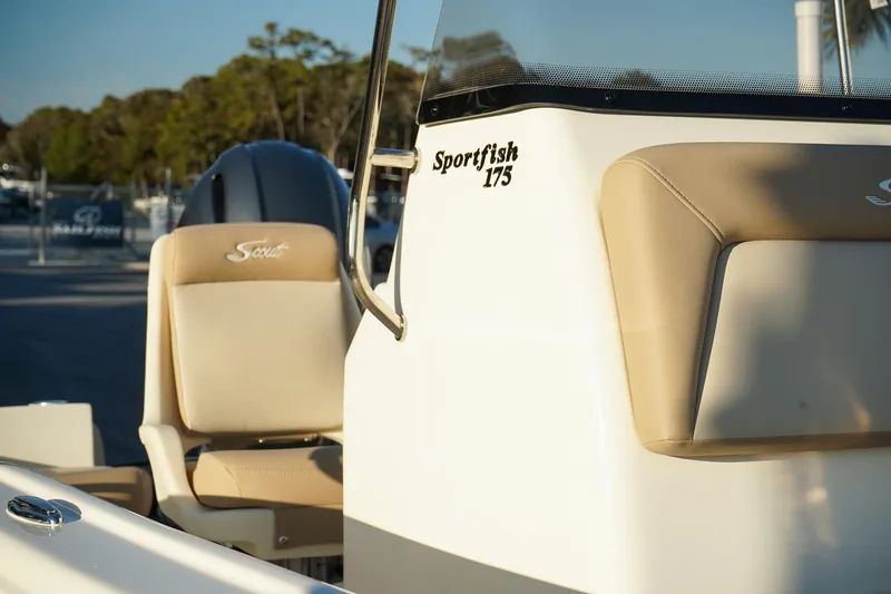 Slide: The Image of 2025 Scout 175 Sportfish boat with beige seating and console, in a marina setting. - 9