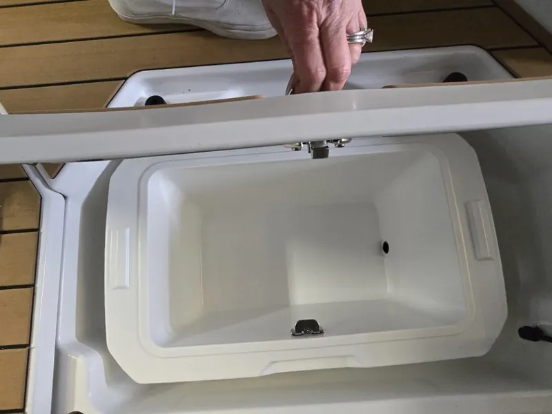 Slide: The Image of 2025 Nautique Super Air Nautique G23 storage compartment with hand opening lid on wooden deck. - 13