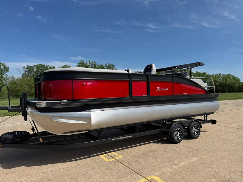 Slide: The Image of 2025 Barletta ARIA 22UC pontoon boat on trailer, red and silver design, parked outdoors. - 3