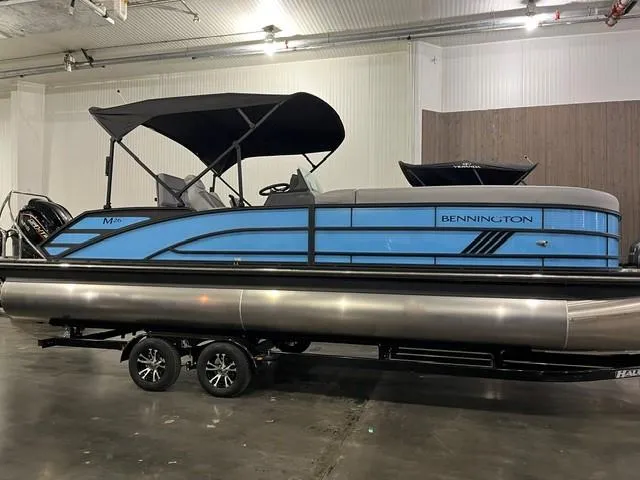 Slide: The Image of 2025 Bennington M 26 Swingback pontoon boat in showroom, featuring sleek blue design. - 6