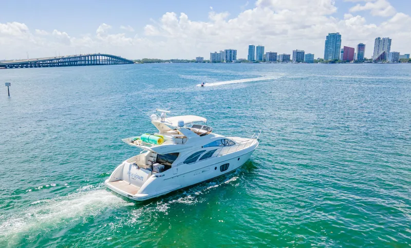 The Image of 2005 Azimut 55E yacht cruising in sunny coastal waters with city skyline backdrop. - 0
