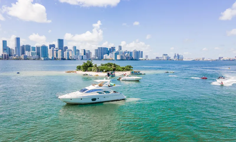 Slide: The Image of Azimut 55E yacht cruising near a small island with city skyline in the background. - 5