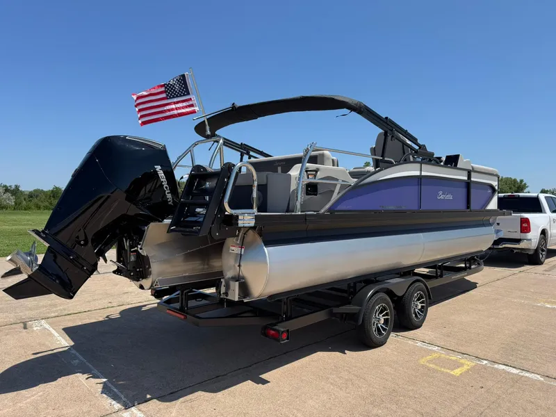 Slide: The Image of 2025 Barletta Cabrio 22UC pontoon boat on trailer with American flag, parked outdoors. - 11