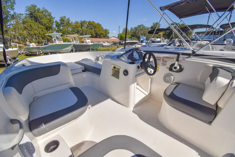 Slide: The Image of 2025 Bayliner E18 boat interior with seating and steering console, docked in a marina. - 5