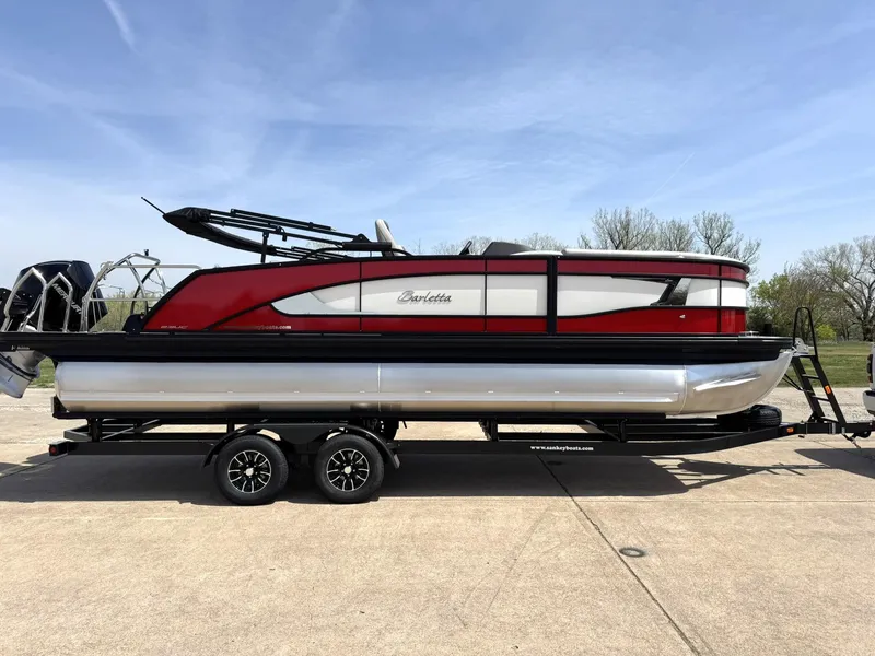 Slide: The Image of 2025 Barletta Lusso 23UC pontoon boat on trailer, red and silver design, parked outdoors. - 11