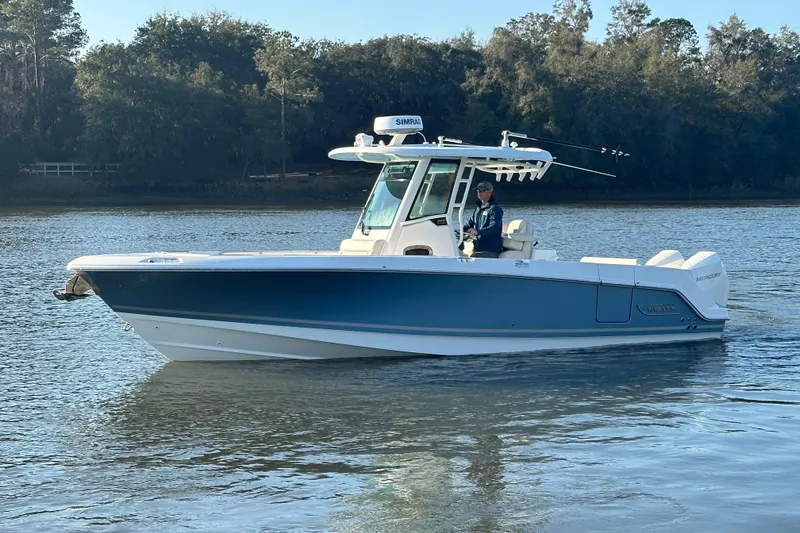 Slide: The Image of 2023 Boston Whaler 280 Outrage boat on calm water, surrounded by trees. - 2