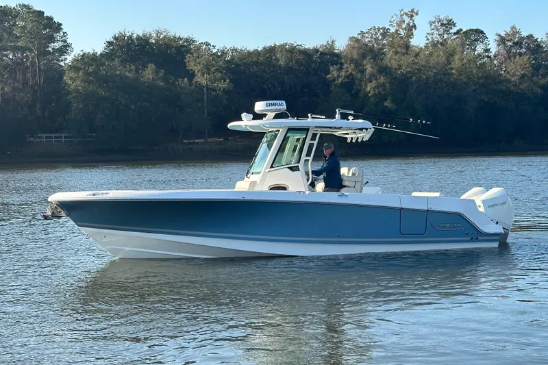 Slide: The Image of 2023 Boston Whaler 280 Outrage boat on calm water, surrounded by trees. - 3