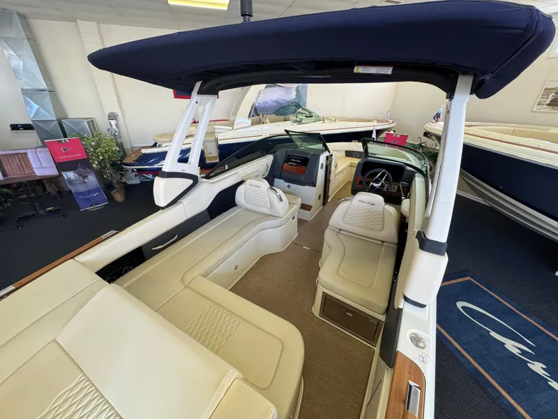 Slide: The Image of 2025 Chris-Craft Sportster 28 interior with beige seating and navy canopy in showroom. - 5