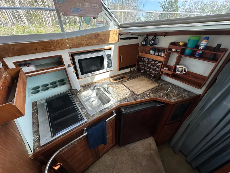 Slide: The Image of 1987 Sea Ray 300 Sedan Bridge kitchen with stove, sink, microwave, and storage shelves. - 18