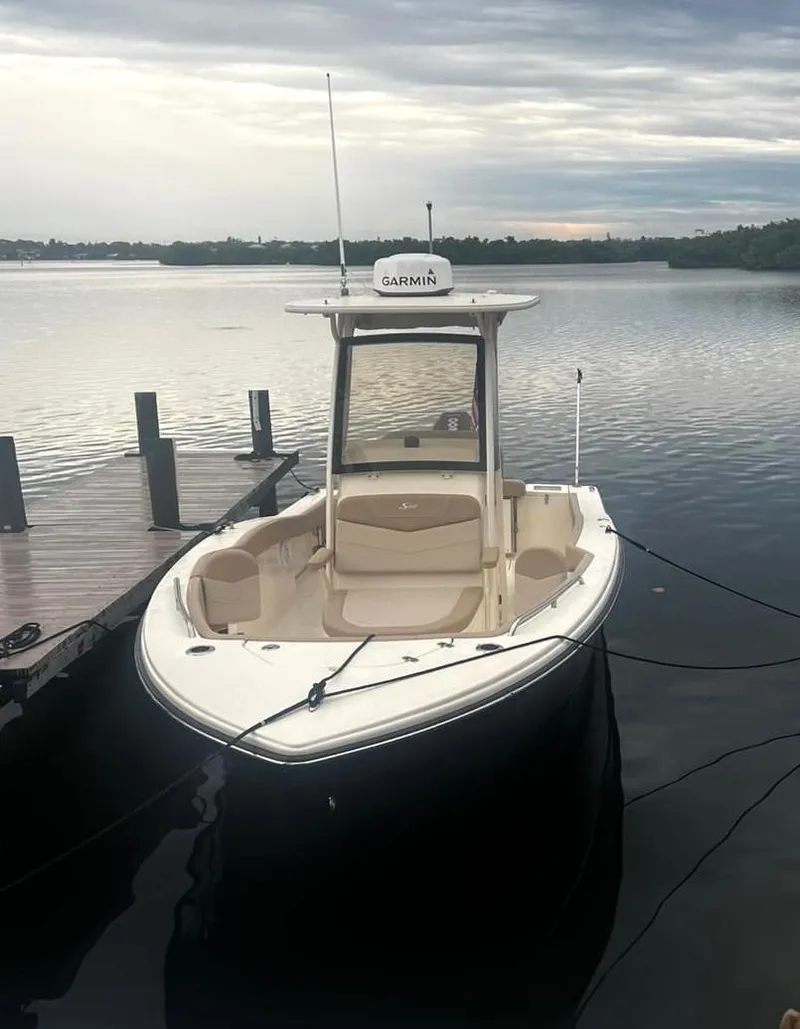 Slide: The Image of 2024 Scout 215 XSF boat docked on calm water under cloudy skies. - 2