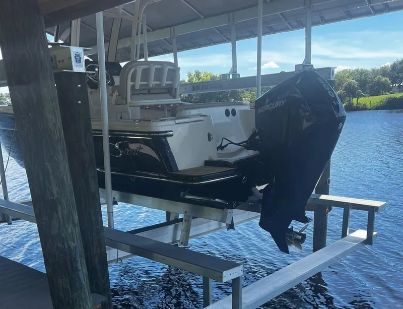 Slide: The Image of 2024 Scout 215 XSF boat on lift, featuring Mercury outboard motor, docked by a serene lake. - 4