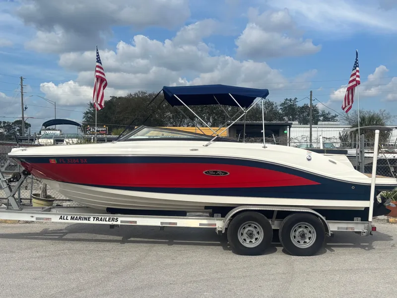 Slide: The Image of 2021 Sea Ray SPX 230 boat on trailer with American flags, under a blue sky. - 2
