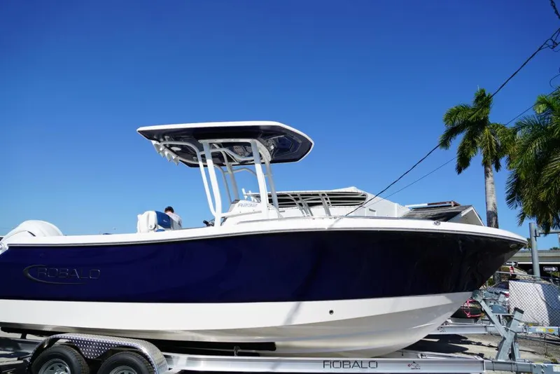 Slide: The Image of 2025 Robalo R232 EX boat on trailer, under clear blue sky, with palm trees. - 28