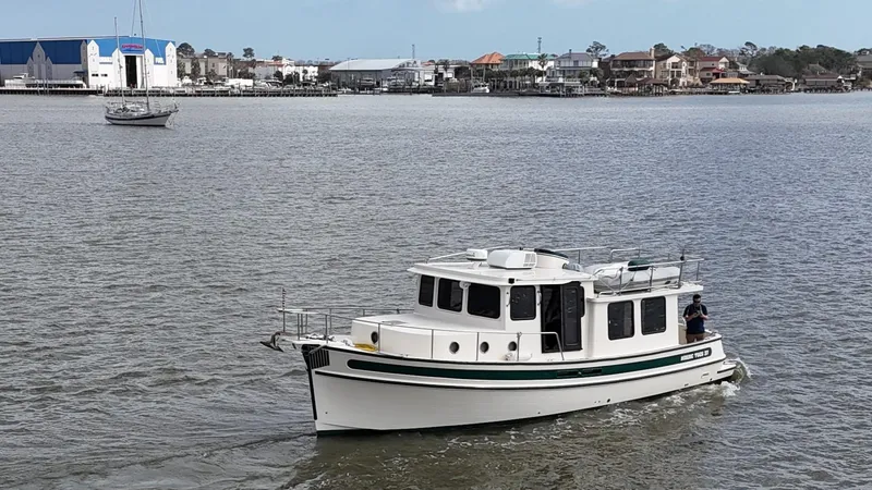 Slide: The Image of 2001 Nordic Tug 37 cruising on a calm river near a coastal town. - 11