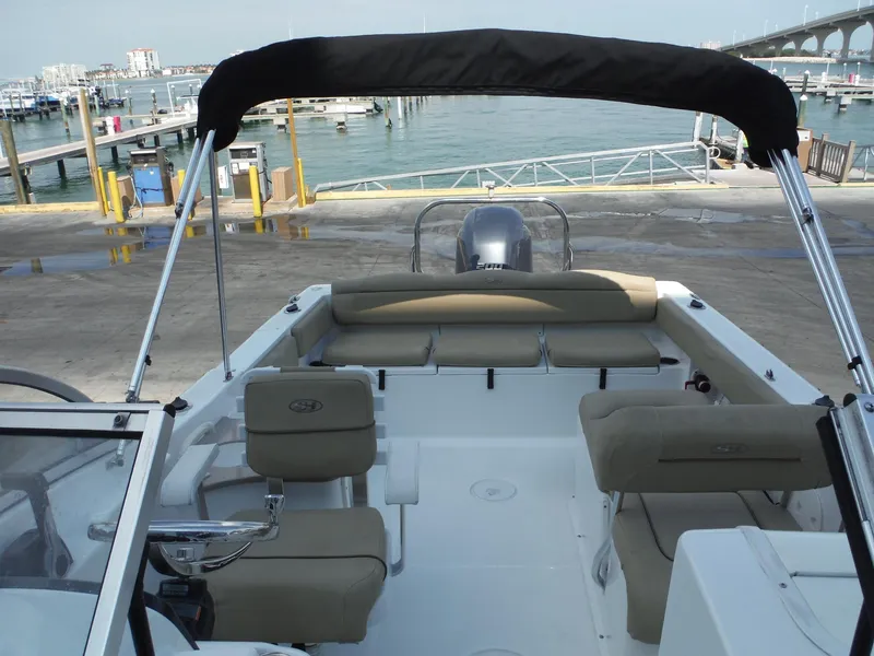 Slide: The Image of 2016 Sea Hunt Escape 235 SE boat interior with seating and canopy at a marina. - 21