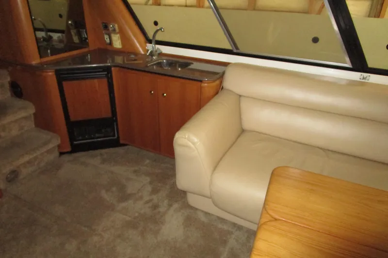 Slide: The Image of 1999 Bayliner 4788 Pilot House Motoryacht interior with beige sofa, kitchenette, and wooden table. - 16