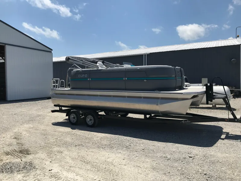 Slide: The Image of 2025 Avalon AURA pontoon boat on trailer, parked near industrial silos and a barn. - 1