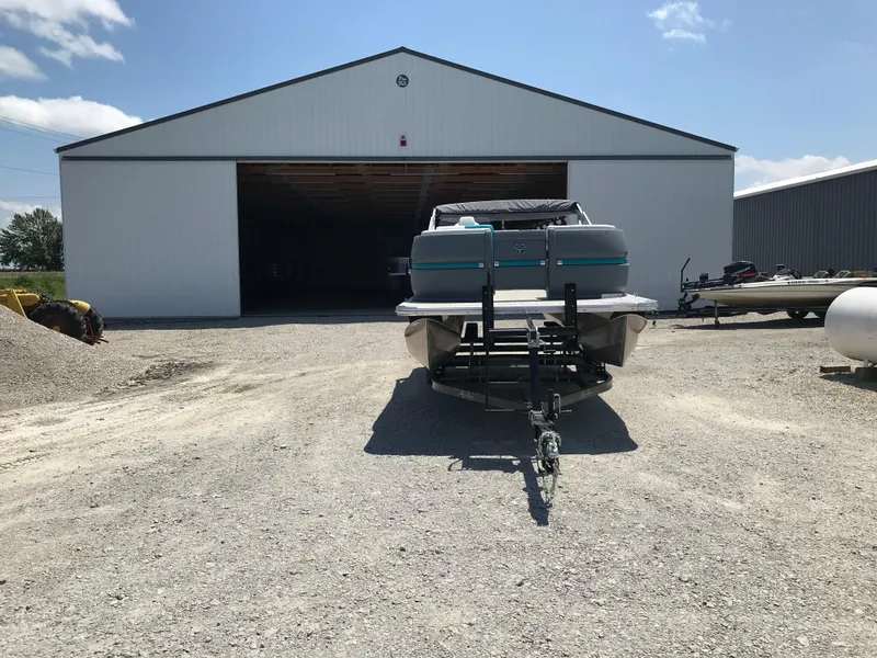 Slide: The Image of 2025 Avalon AURA pontoon boat on trailer, parked outside a building under a clear blue sky. - 3