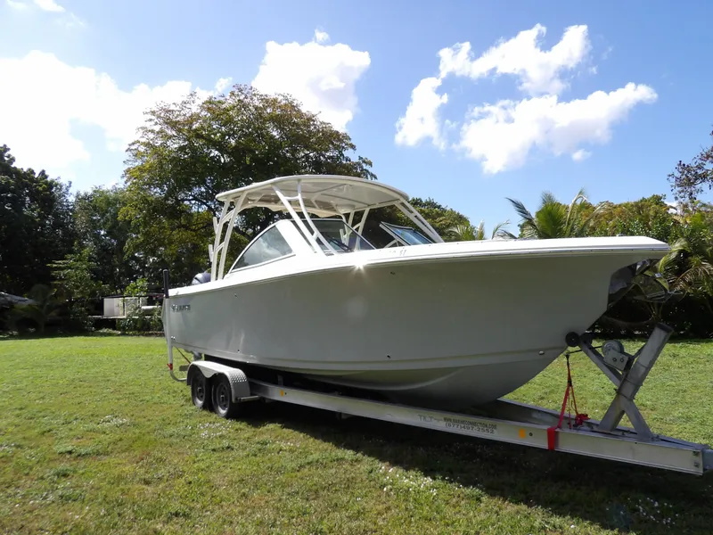 Slide: The Image of 2020 Sailfish 275 DC boat on trailer, parked on grass under a sunny sky. - 3