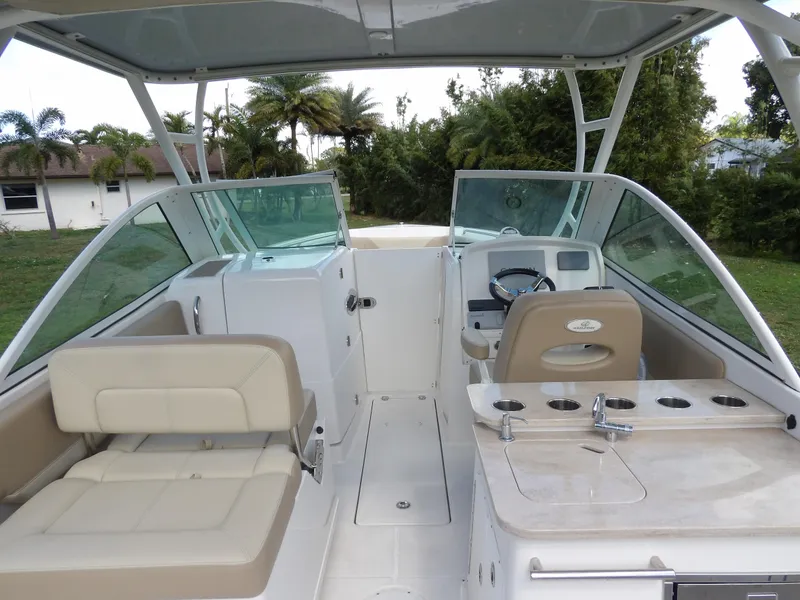 Slide: The Image of 2020 Sailfish 275 DC boat interior with seating and helm, surrounded by lush greenery. - 34