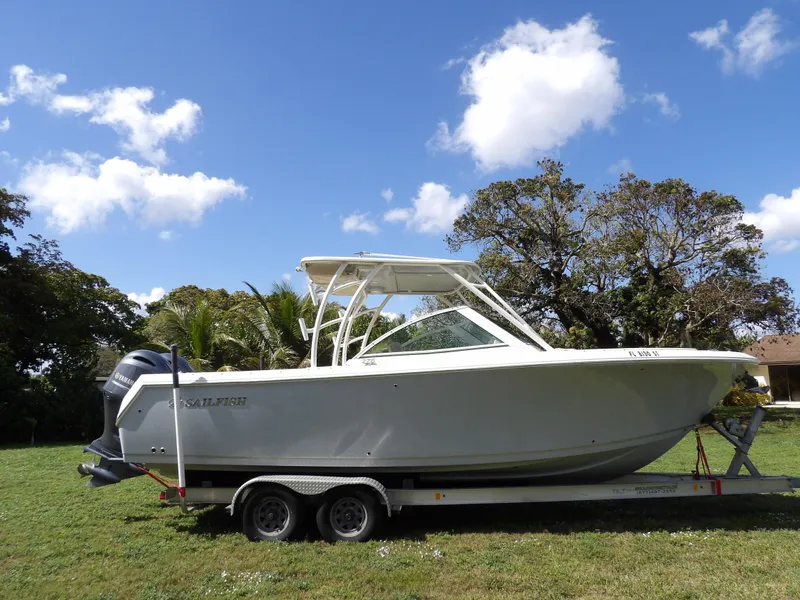 Slide: The Image of 2020 Sailfish 275 DC boat on trailer, parked on grass under a clear blue sky. - 5