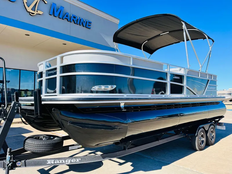 Slide: The Image of 2025 Ranger Reata 223C pontoon boat on trailer outside marine dealership. - 2
