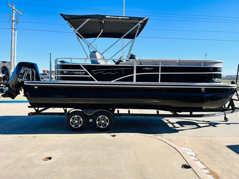 Slide: The Image of 2025 Ranger Reata 223C pontoon boat on trailer, black exterior, sunny day. - 4