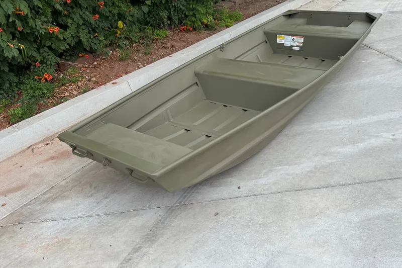 The Image of 2025 Tracker Grizzly 14 Jon boat on concrete, surrounded by greenery. - 0