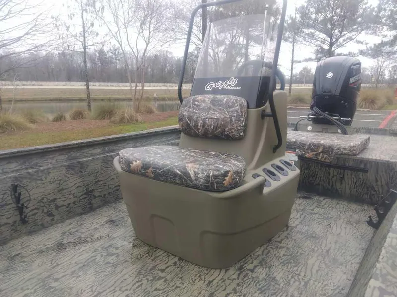 Slide: The Image of 2025 Tracker Grizzly 1860 CC boat with camo seats and console, parked near a lake. - 9