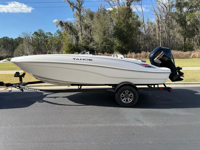Slide: The Image of 2025 Tahoe T18 boat on trailer, parked outdoors, clear sky, trees in background. - 0