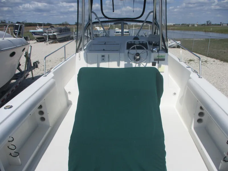 Slide: The Image of 2001 Shamrock 246 Walkaround boat with green cover, docked outdoors under a cloudy sky. - 8
