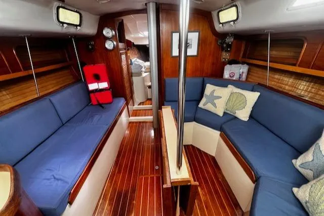 Slide: The Image of 1988 CAL Sloop interior with blue seating, wooden flooring, and nautical decor. - 1
